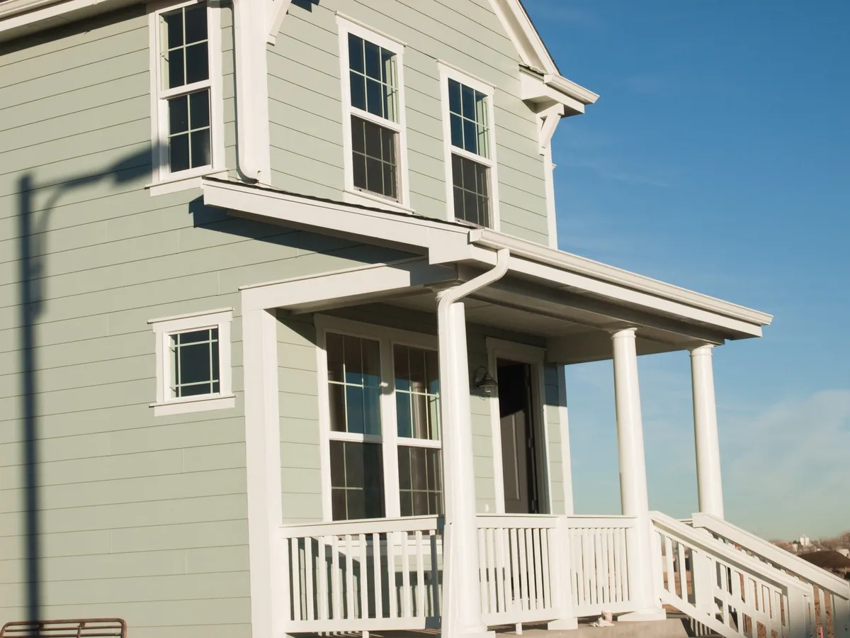 Exterior of a house with green siding, large windows, and a front porch with a ramp.