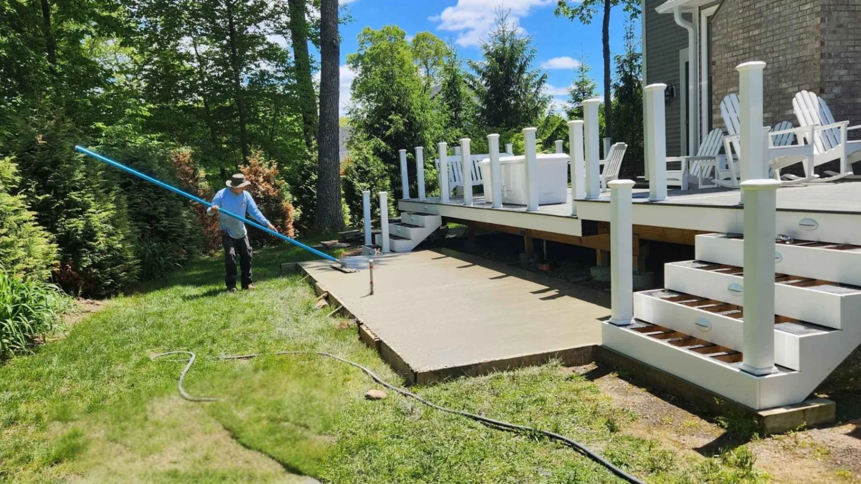 A contractor smoothing freshly poured concrete for a new patio beside a raised deck, part of our landscaping services offered in New Milford, CT.