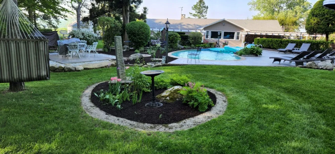 A landscaped backyard with a circular garden bed, fresh mulch, and a birdbath centered in a manicured lawn near a pool and patio area in Westport, CT.