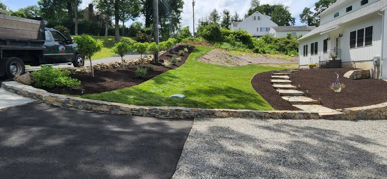 A sloped backyard with fresh sod, curved mulch beds, stone retaining walls, and natural stone steps, completed as part of a landscaping project in Westport, CT.
