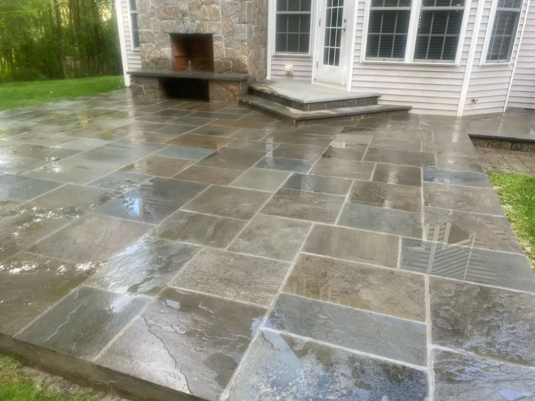 A newly installed stone patio featuring large rectangular slate tiles and a custom stone fireplace, creating a sleek and modern outdoor living space at a home in Wilton, CT.