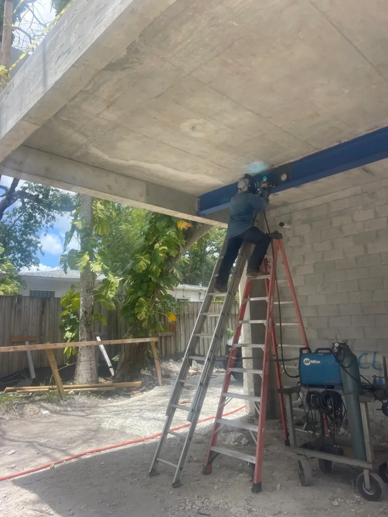 An AWS-certified welder from Abel Welding Services on a ladder installing a structural steel I-beam for a building construction project in Hollywood, FL.