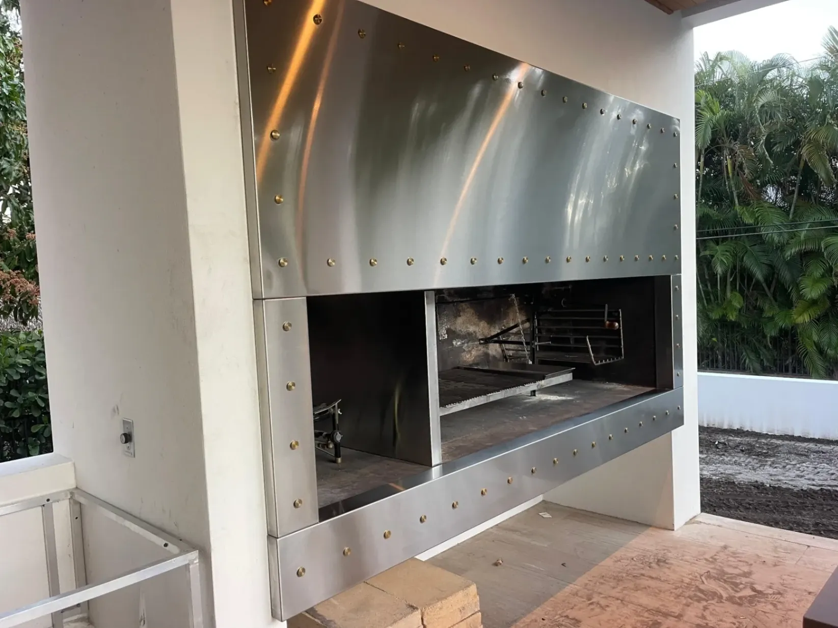 Custom stainless steel Argentine-style grill enclosure with brass rivet accents, expertly built by our master metal fabricators in Deerfield Beach for an upscale outdoor kitchen.