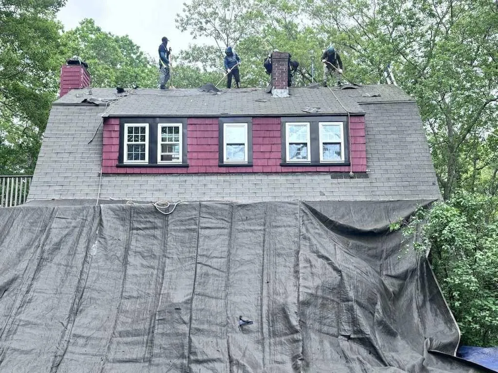 JM Exteriors Roofing Siding's roofing team performing a full roof replacement in Westford, MA, featuring a 10-year labor warranty and property protection with heavy-duty tarps.