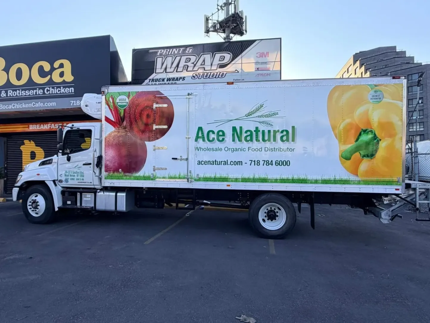 Custom vinyl box truck wrap for Ace Natural featuring photorealistic beet and yellow pepper graphics, printed and installed by Print & Wrap Studio Corp. The high-resolution wrap covers a white Hino delivery truck parked in front of the studio's location.