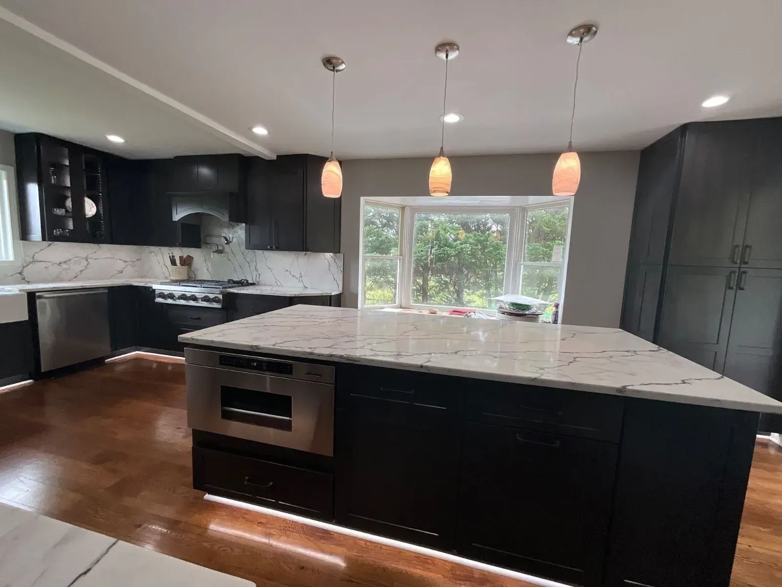 Premium white quartz countertop installation with bold gray veining in a Fairfax kitchen remodel, featuring a large black kitchen island, matching full-height slab backsplash, custom dark cabinetry, glowing toe-kick lighting, and warm pendant lights.