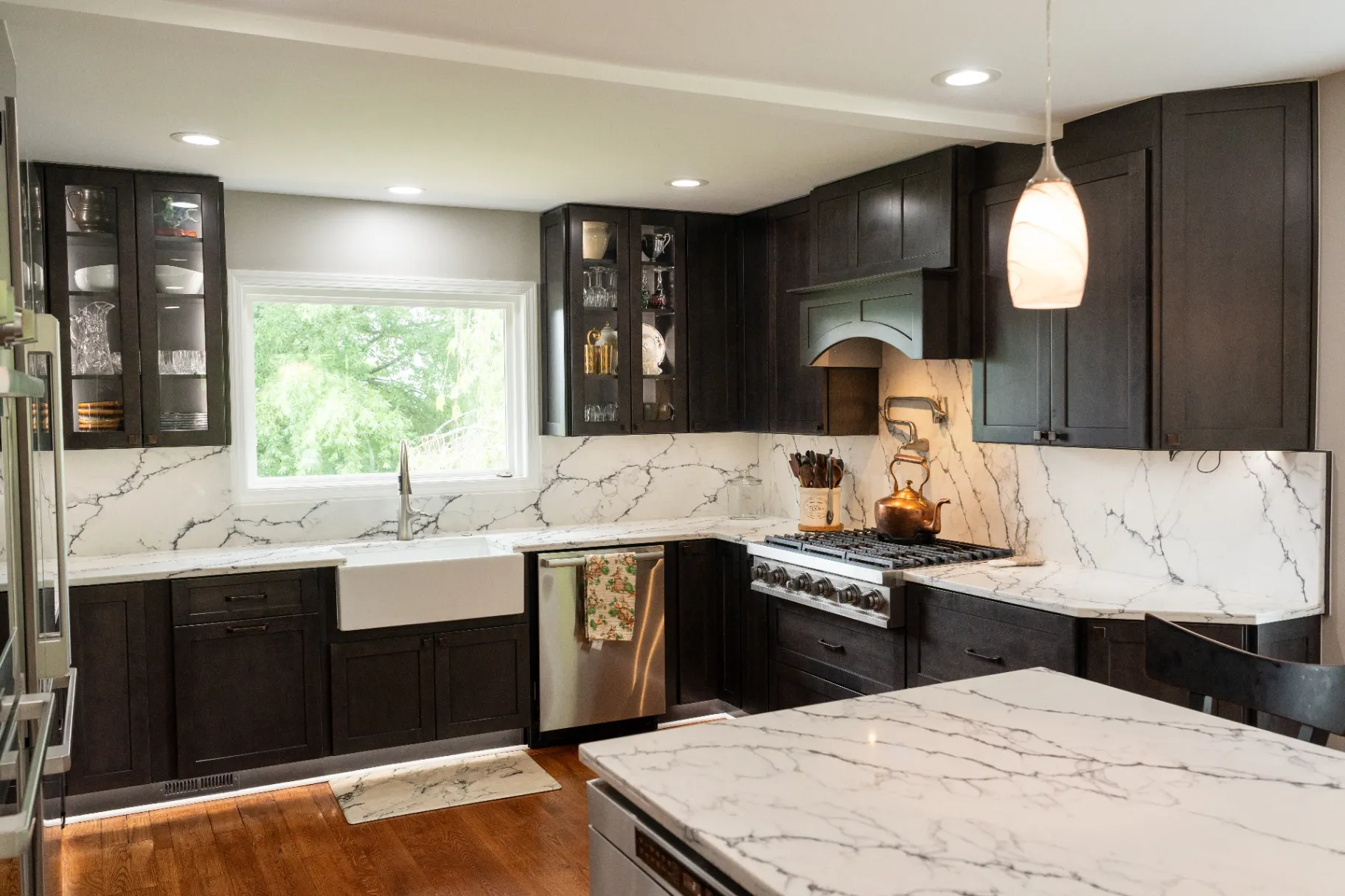 A modern kitchen remodel by KBA Kitchen and Bath (Class-A licensed kitchen remodeler in Fairfax, VA) featuring light gray floor-to-ceiling cabinets, white quartz countertops, a honeycomb hexagon tile backsplash, and large marble-look floor tiles.