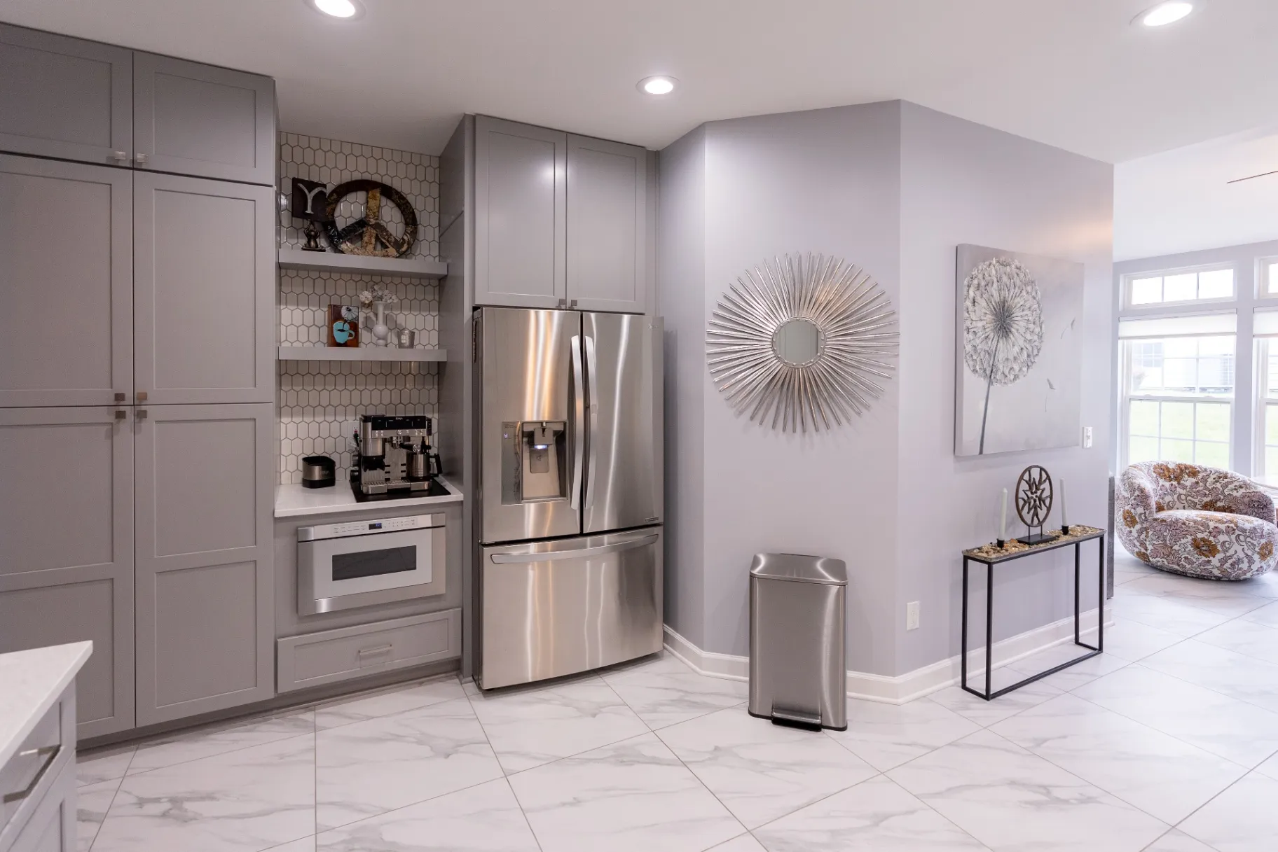 Modern kitchen remodel in Fairfax completed by KBA Kitchen and Bath Design and Build featuring a large dark gray island with a white quartz countertop, custom white shaker cabinets, a mosaic stone backsplash, stainless steel appliances, and elegant pendant lighting design.