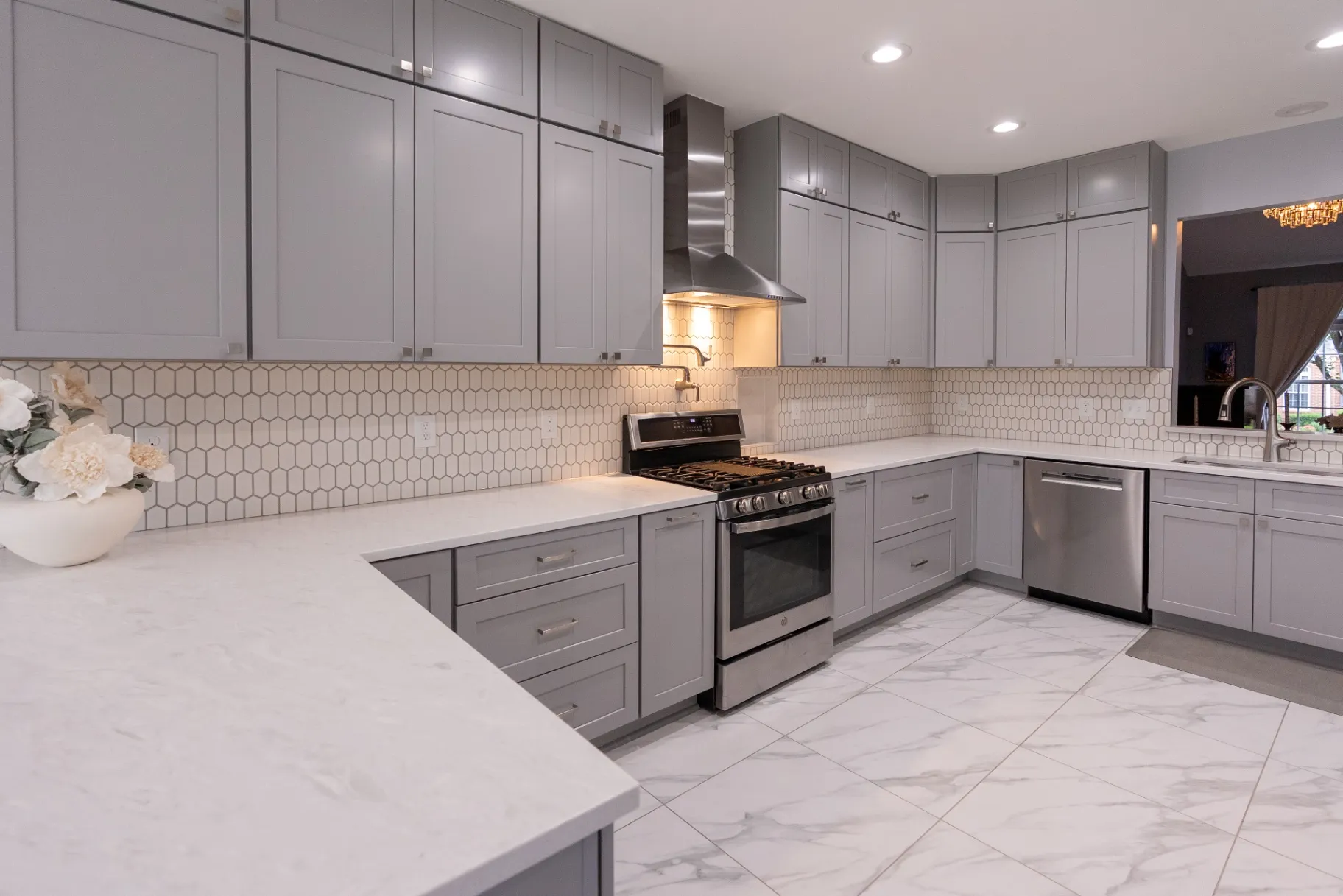 Premium engineered hardwood floor installation in a luxury kitchen remodeling in Fairfax, featuring a large marble-look quartz island with seating, a mix of natural wood and white shaker cabinets, and recessed lighting.