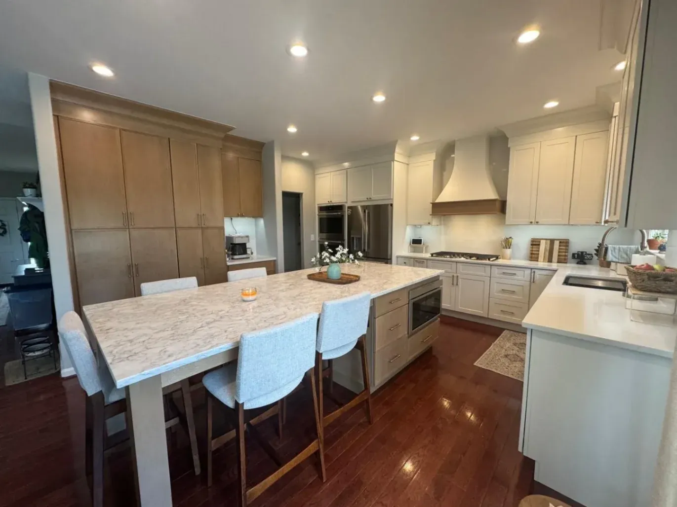 Premium engineered hardwood floor installation in a luxury kitchen remodeling in Fairfax, featuring a large marble-look quartz island with seating, a mix of natural wood and white shaker cabinets, and recessed lighting.