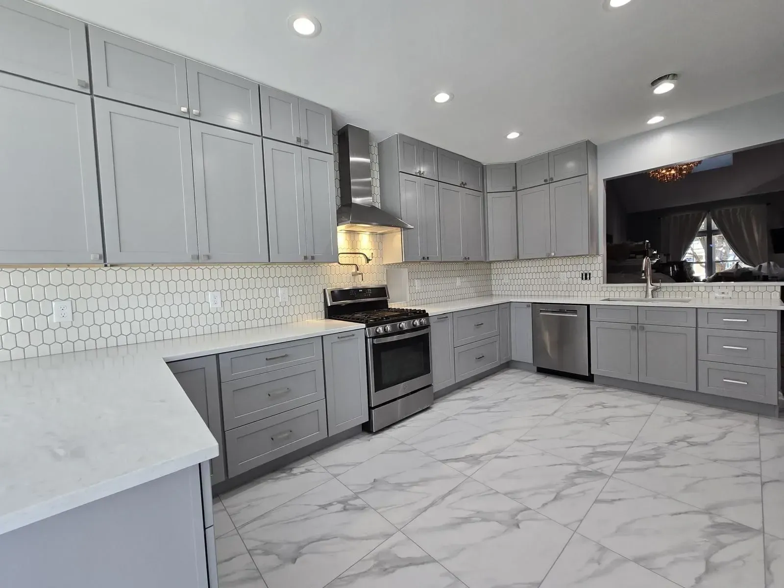 A modern kitchen remodel by KBA Kitchen and Bath (Class-A licensed kitchen remodeler in Fairfax, VA) featuring light gray floor-to-ceiling cabinets, white quartz countertops, a honeycomb hexagon tile backsplash, and large marble-look floor tiles.