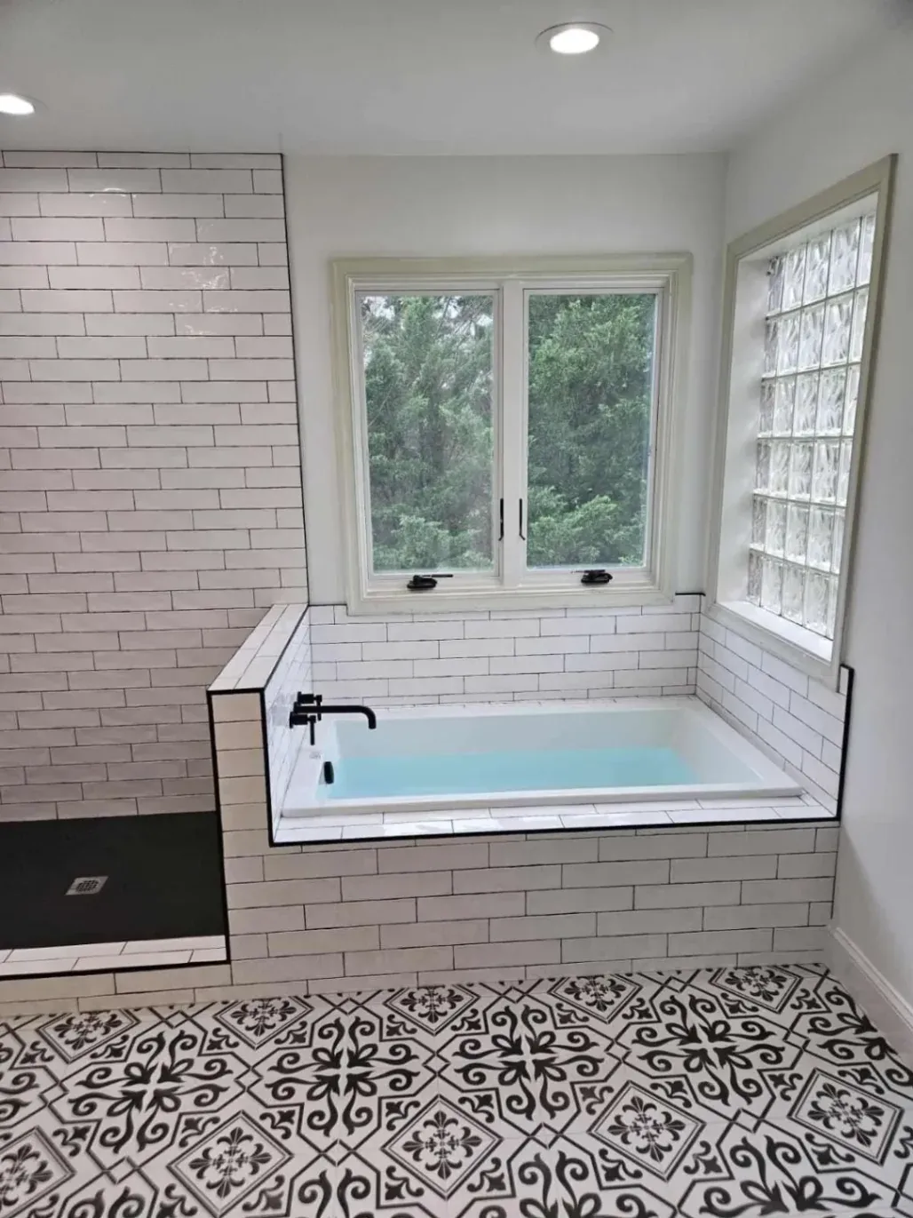 Luxury bathroom remodeling in Fairfax featuring elegant black and white patterned floor tiles and a white subway tile soaking tub surround.