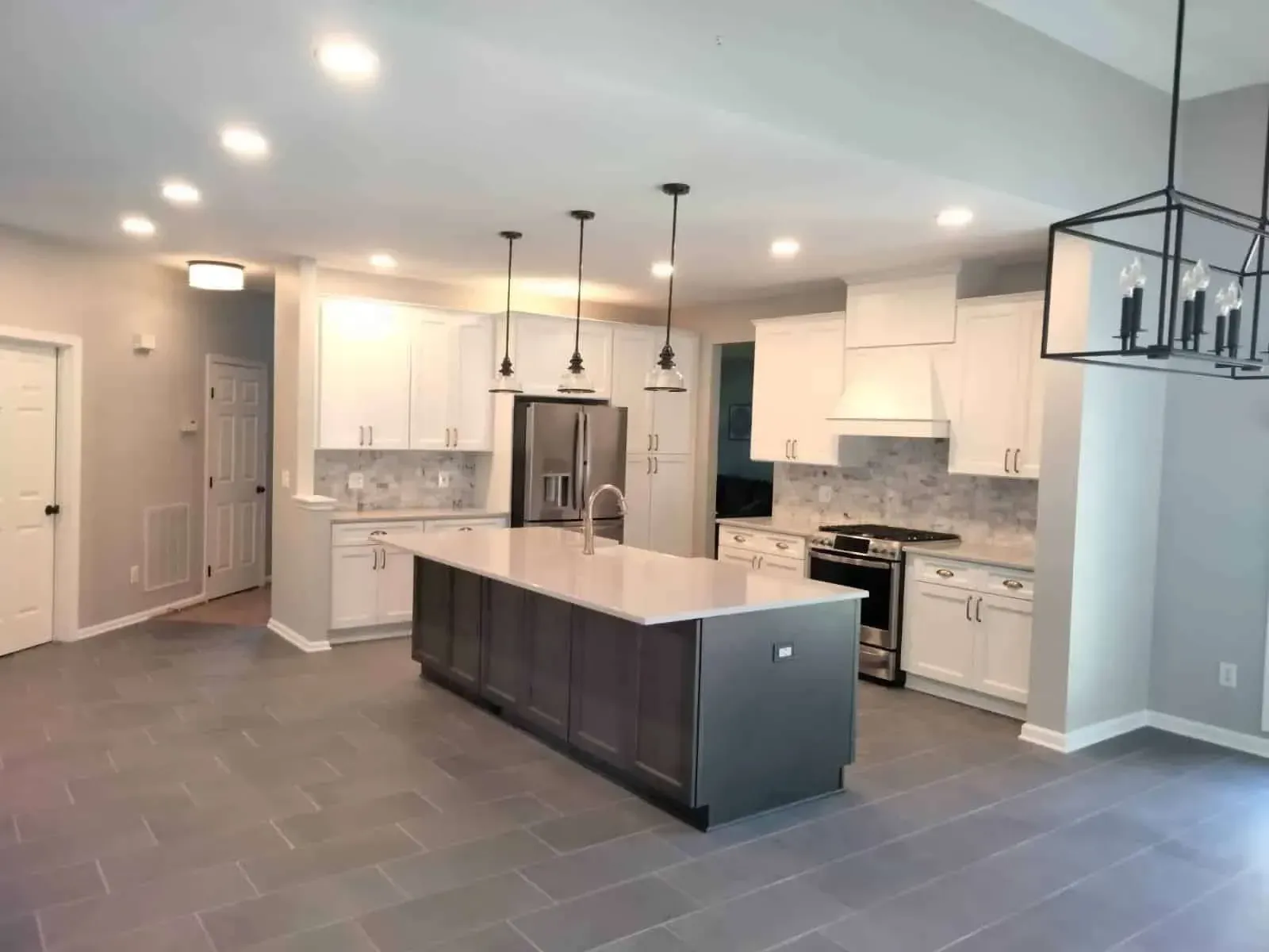 Modern kitchen remodel in Fairfax completed by KBA Kitchen and Bath Design and Build featuring a large dark gray island with a white quartz countertop, custom white shaker cabinets, a mosaic stone backsplash, stainless steel appliances, and elegant pendant lighting design.