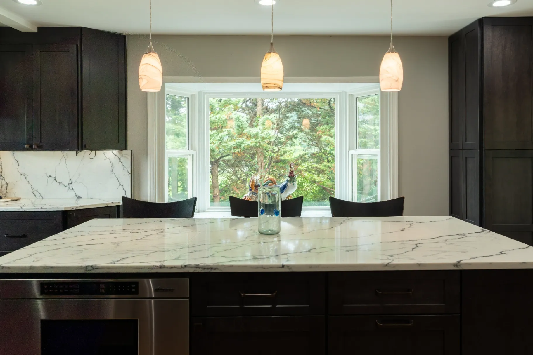 Premium white quartz countertop installation with bold gray veining in a Fairfax kitchen remodel, featuring a large black kitchen island, matching full-height slab backsplash, custom dark cabinetry, glowing toe-kick lighting, and warm pendant lights.
