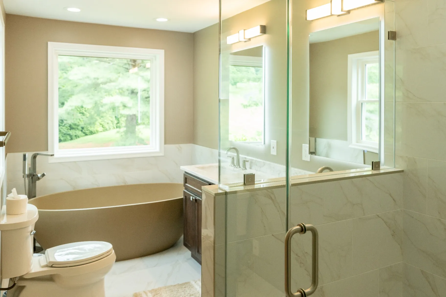 A modern luxury walk-in shower with a frameless glass enclosure, featuring gray and blue wood-look wall tiles, a natural pebble stone floor, a matching built-in shower bench, and premium matte black shower fixtures with body jets. This is the result of a bathroom remodeling in Fairfax, VA.