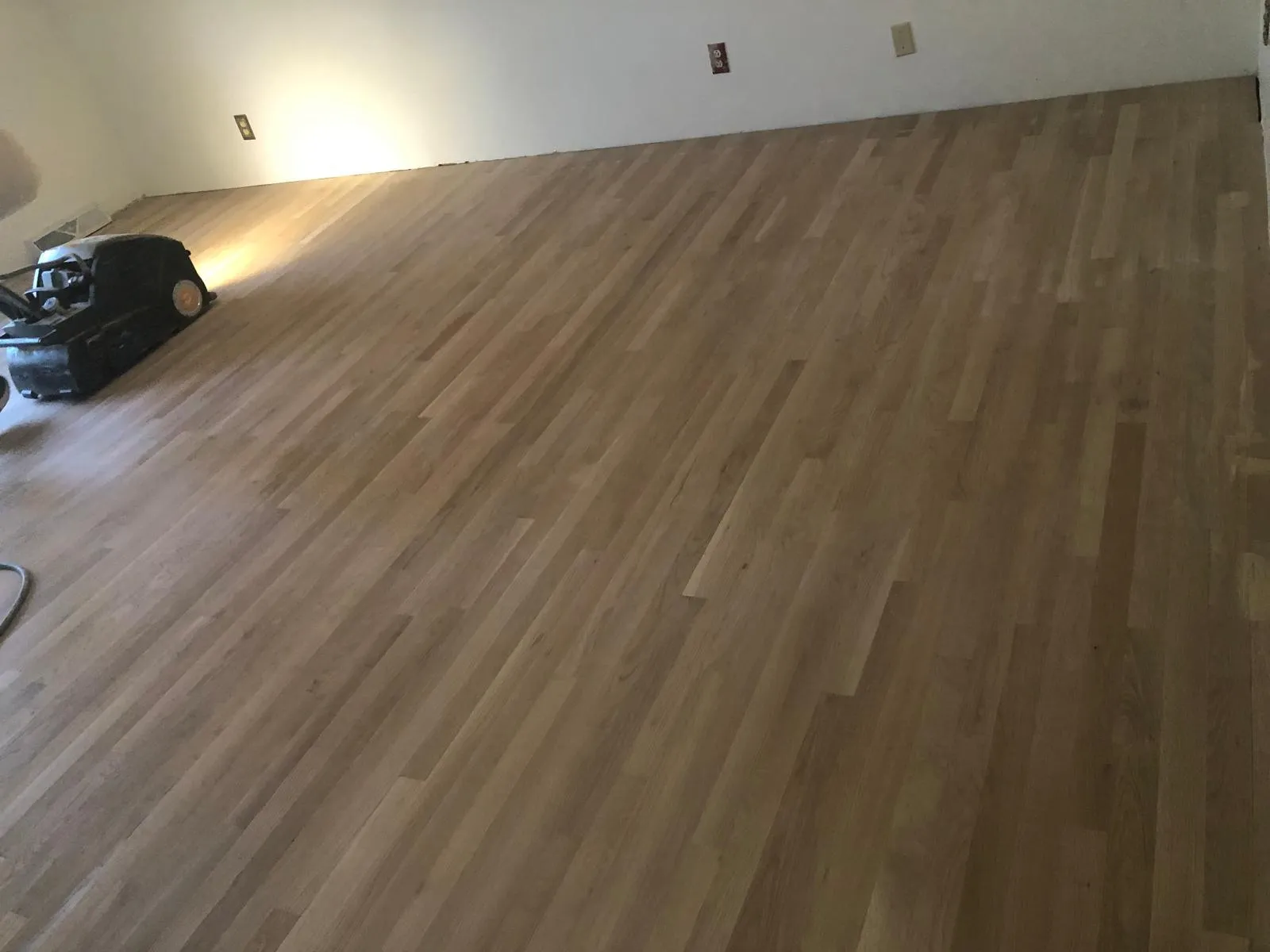 Hardwood floor sanding machine removing scratches during a refinishing project by DNH Hardwood Flooring in Apex, NC.