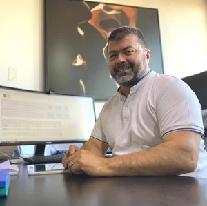 Certo, ecco una didascalia per l'immagine:

"Un uomo d'affari sorridente è seduto alla sua scrivania davanti a un computer e un tablet. L'immagine trasmette un senso di professionalità e successo."