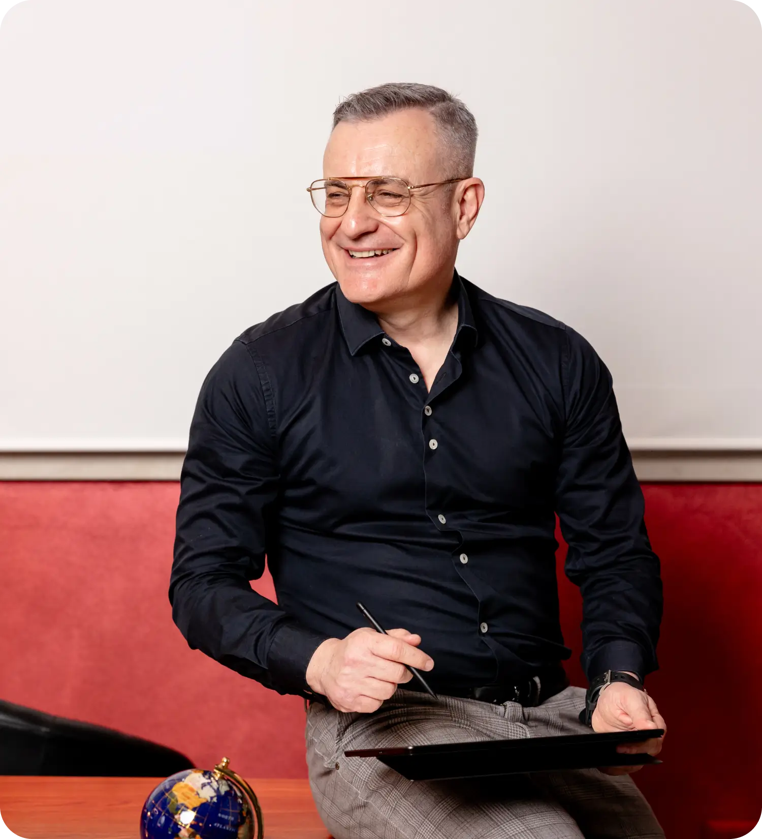Uomo sorridente seduto su una scrivania con tavoletta e penna.