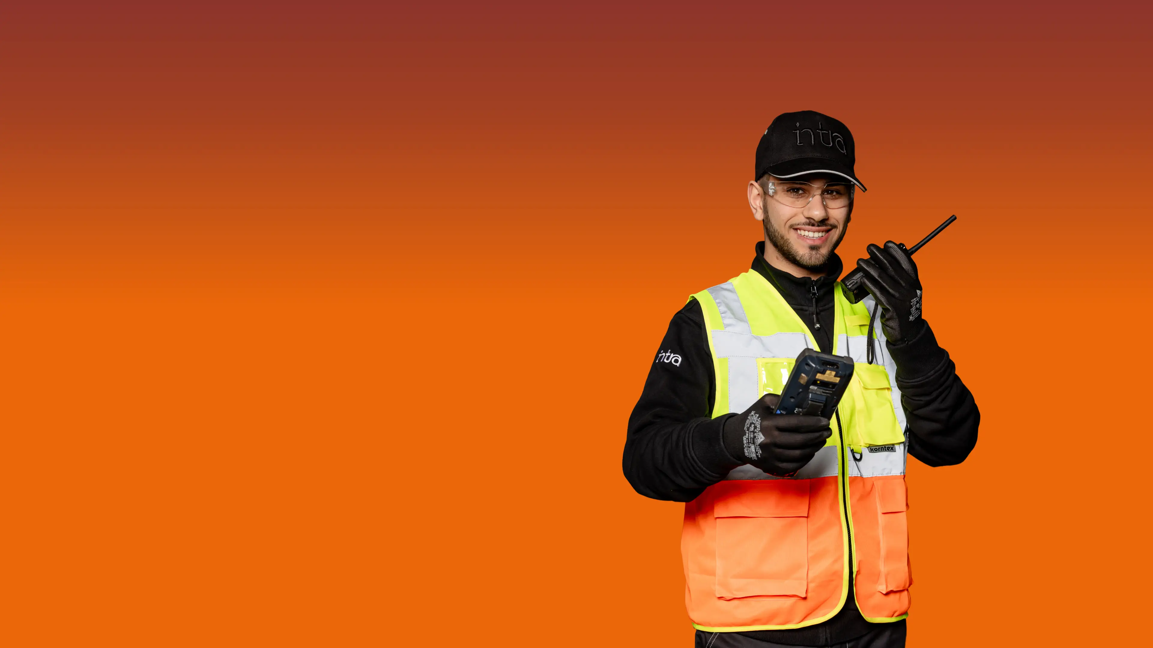 Un uomo sorridente con abbigliamento ad alta visibilità tiene in mano una radio e un dispositivo.