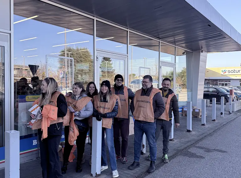 Un gruppo di volontari posa davanti a un negozio indossando gilet arancioni con la scritta "Volontario".