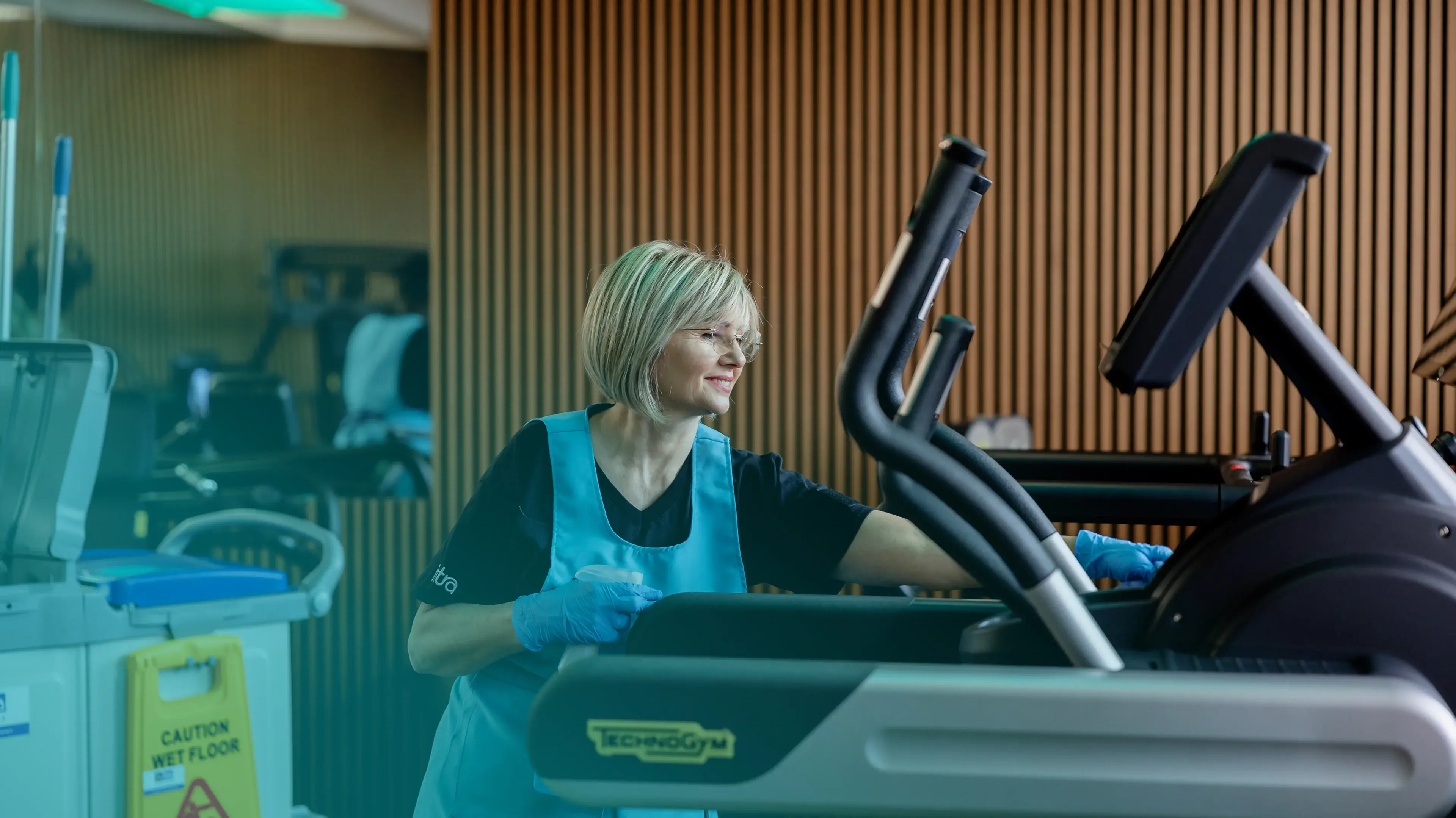 Una donna pulisce un tapis roulant in palestra.