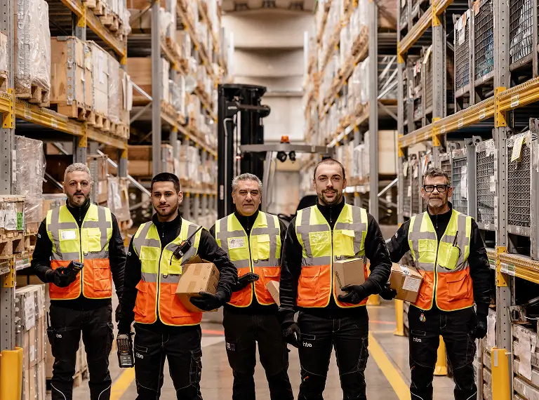 Magazzinieri in fila con indumenti da lavoro e scatole in mano.