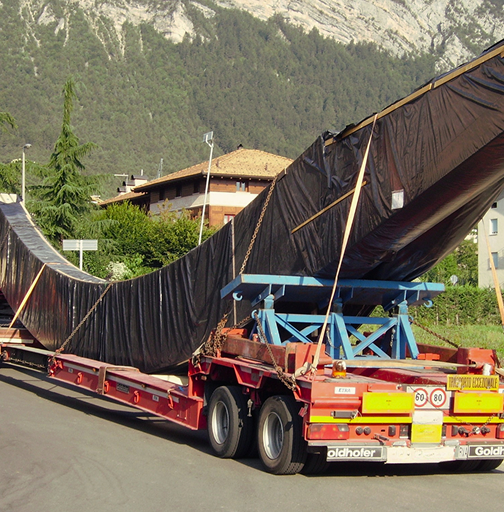 Trasporto eccezionale di un manufatto curvo su rimorchio Goldhofer, tra le montagne.