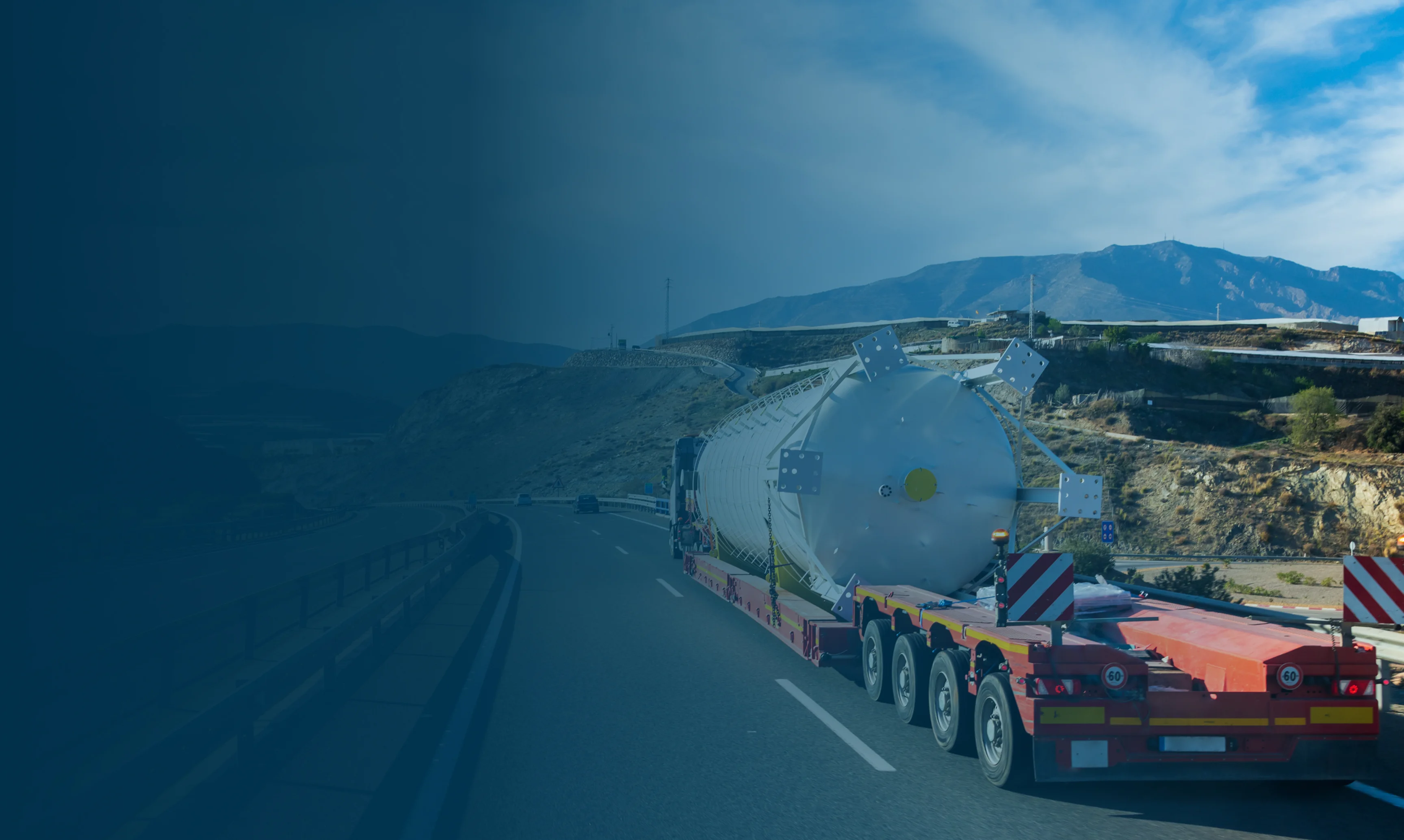 Gigantesco serbatoio bianco su trasporto eccezionale lungo una strada montana sotto un cielo azzurro.