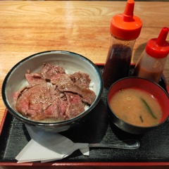 A bowl of rice topped with several thin slices of steak meat