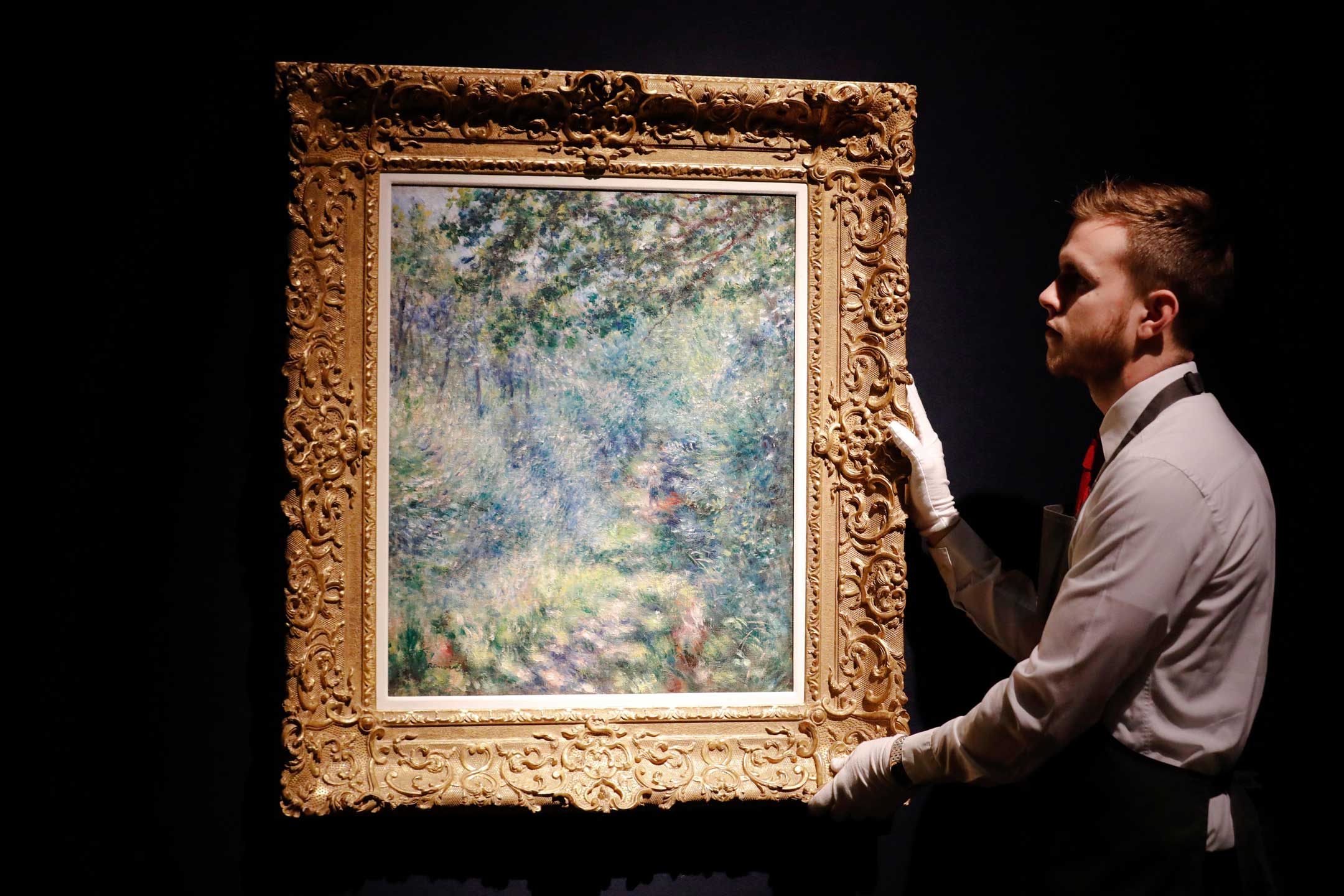 Christie’s Auction House, London, UK. 21st Feb 2019. A Christie’s employee poses with artwork “Sentier dans le bois” by Pierre-Auguste Renoir at Christie’s Auction House in London, Thursday February 21, 2019.