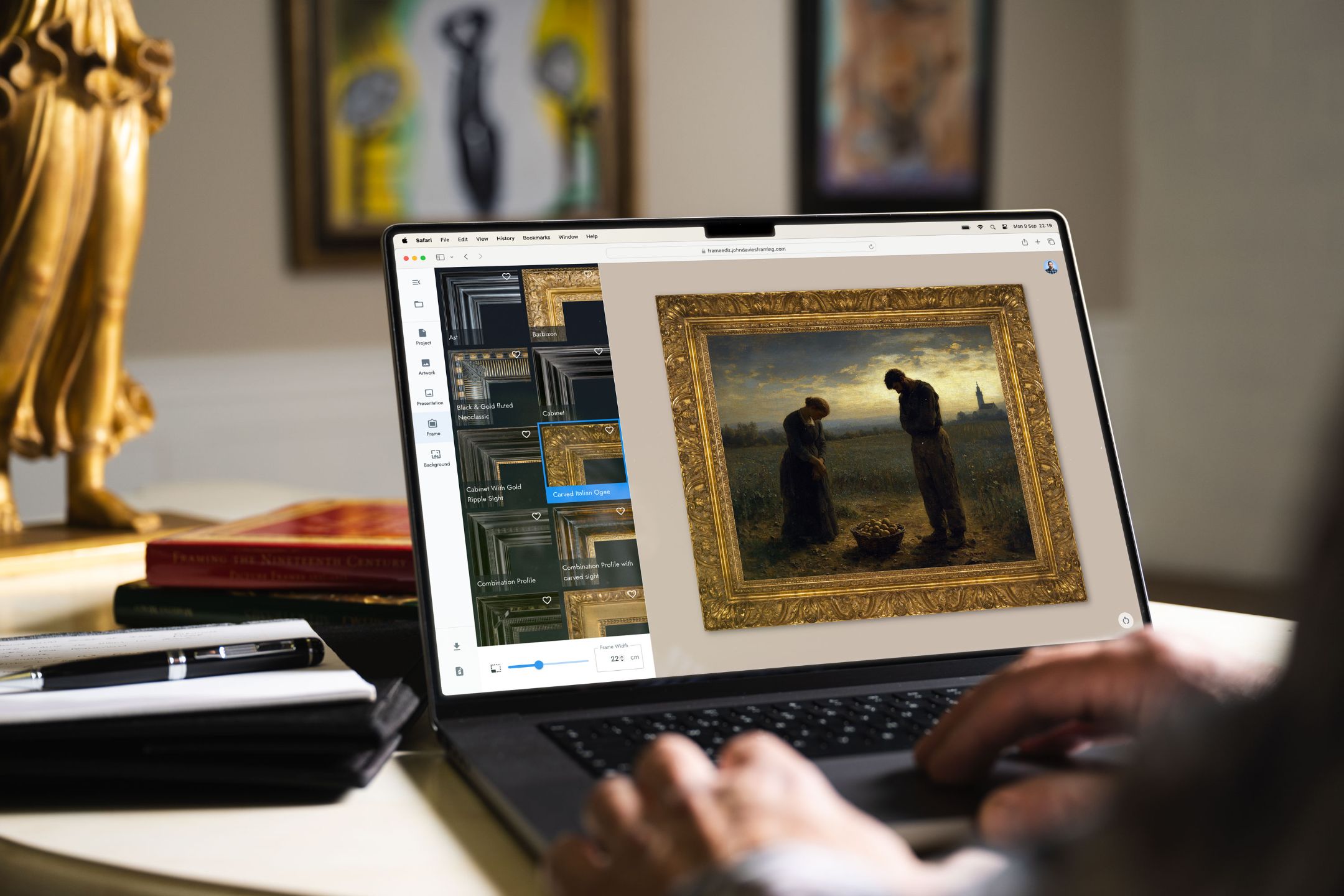 Person editing a framed painting on a laptop with art and books nearby.