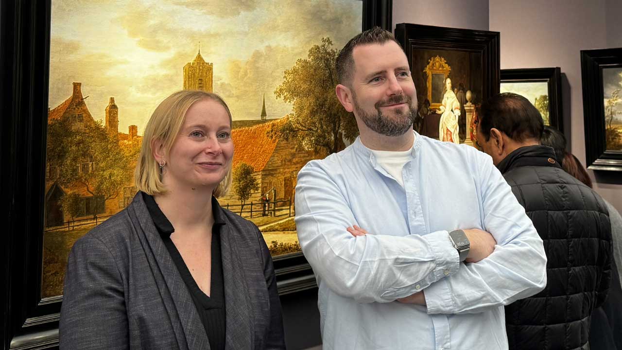 Two people standing in an art gallery, with paintings displayed on the walls.