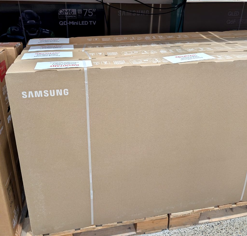 Large Samsung 65-inch 4K UHD MiniLED TV in its original beige cardboard box from Costco, priced at $1396.99.