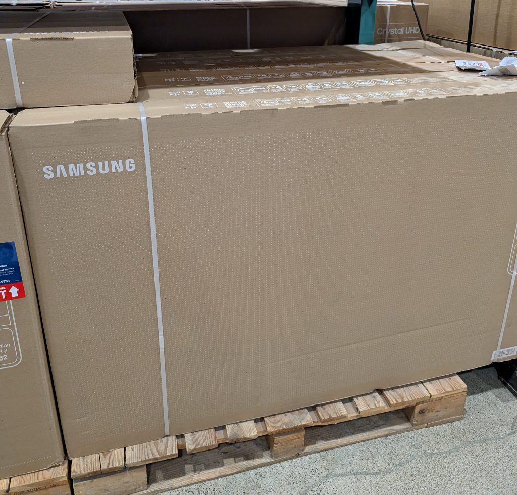 Large Samsung 65" 4K UHD QLED TV in its shipping box from Costco, priced at $996.99 for a premium home entertainment experience.