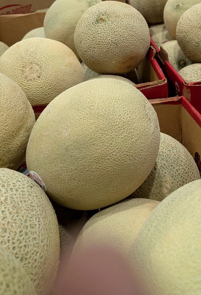 Fresh, light green cantaloupes displayed in bulk boxes at Costco for $3.99, perfect for a refreshing snack.