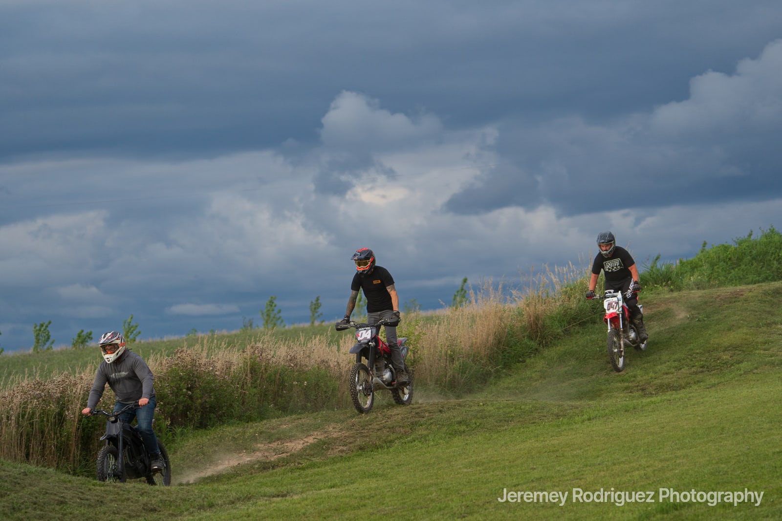 Three Dirt Bike Riders on a Grassy Track