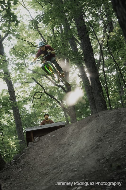 Mountain Biker Launching Through Sunlit Trees