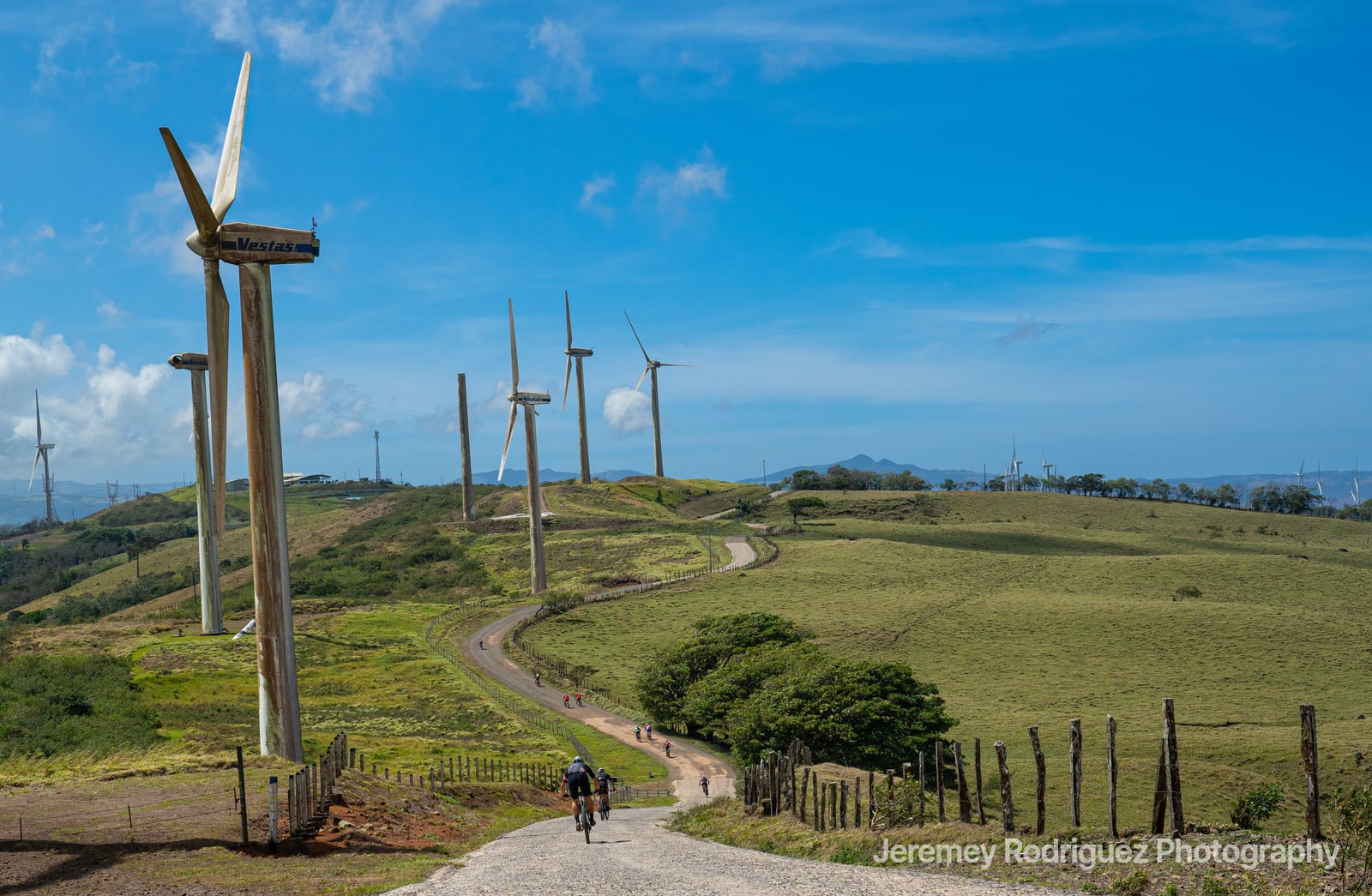 Riders on Rolling Farm Roads Under Turbines