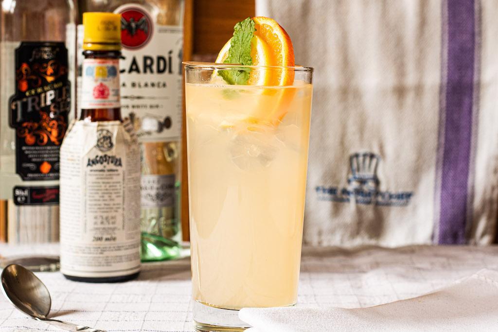 Añejo Highball cocktail in a tall glass with ice, orange and lime wedge garnish