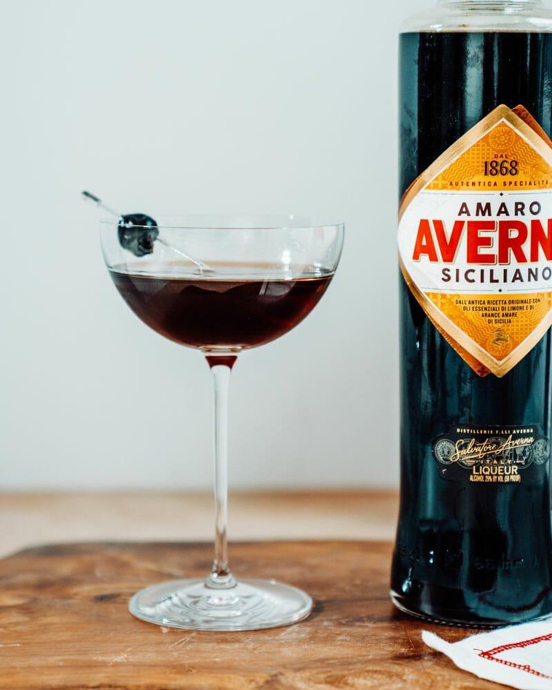 Black Manhattan cocktail in a coupe glass with cocktail cherry garnish