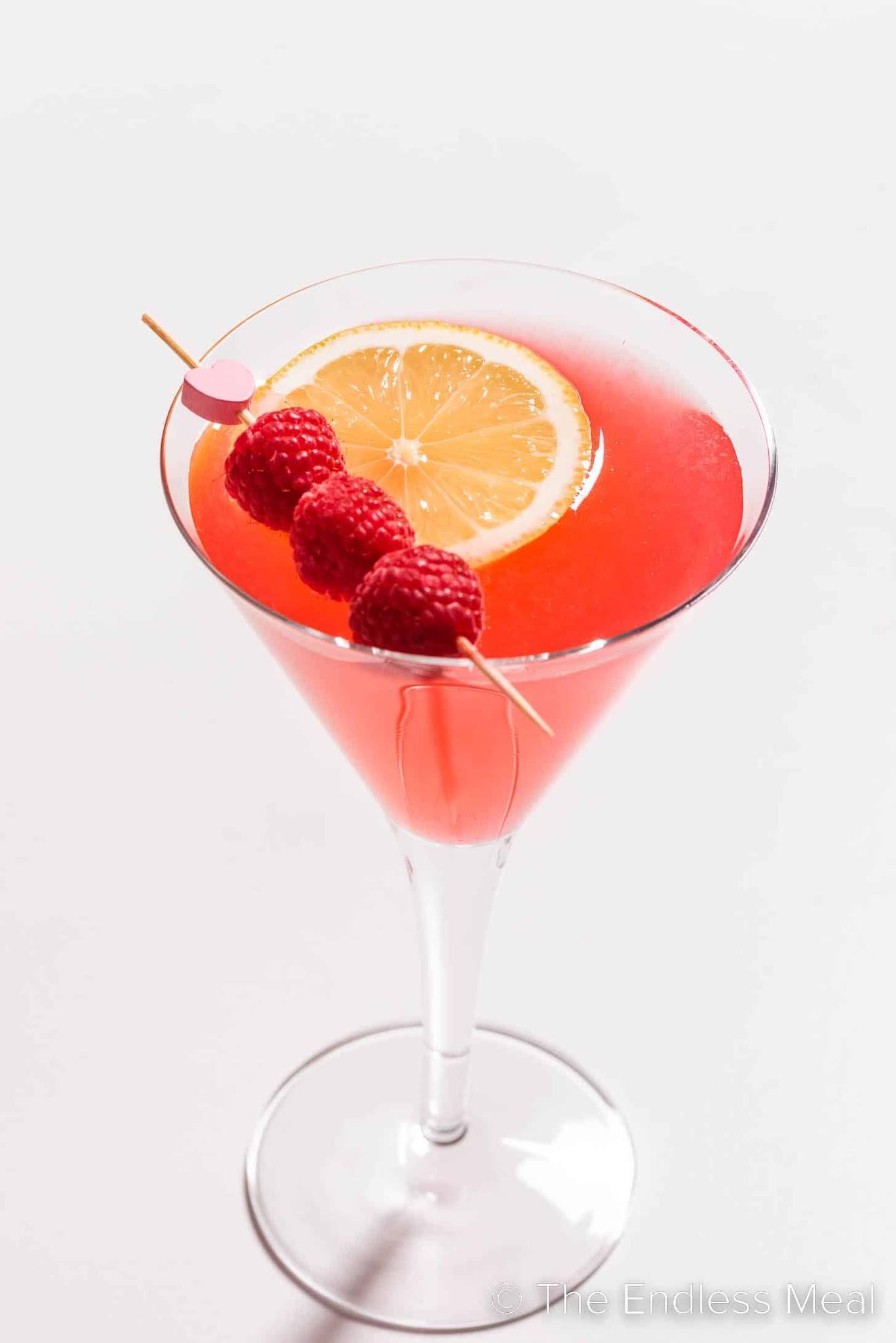1934 COSMO cocktail in a martini glass with lemon peel and raspberry garnish