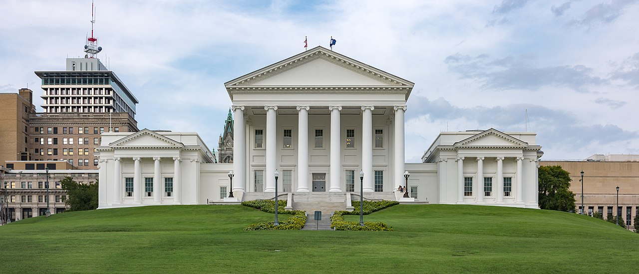Front view of the Virginia State Capitol building in Richmond, Virginia, with a well-manicured lawn and a cloudy sky in the background.