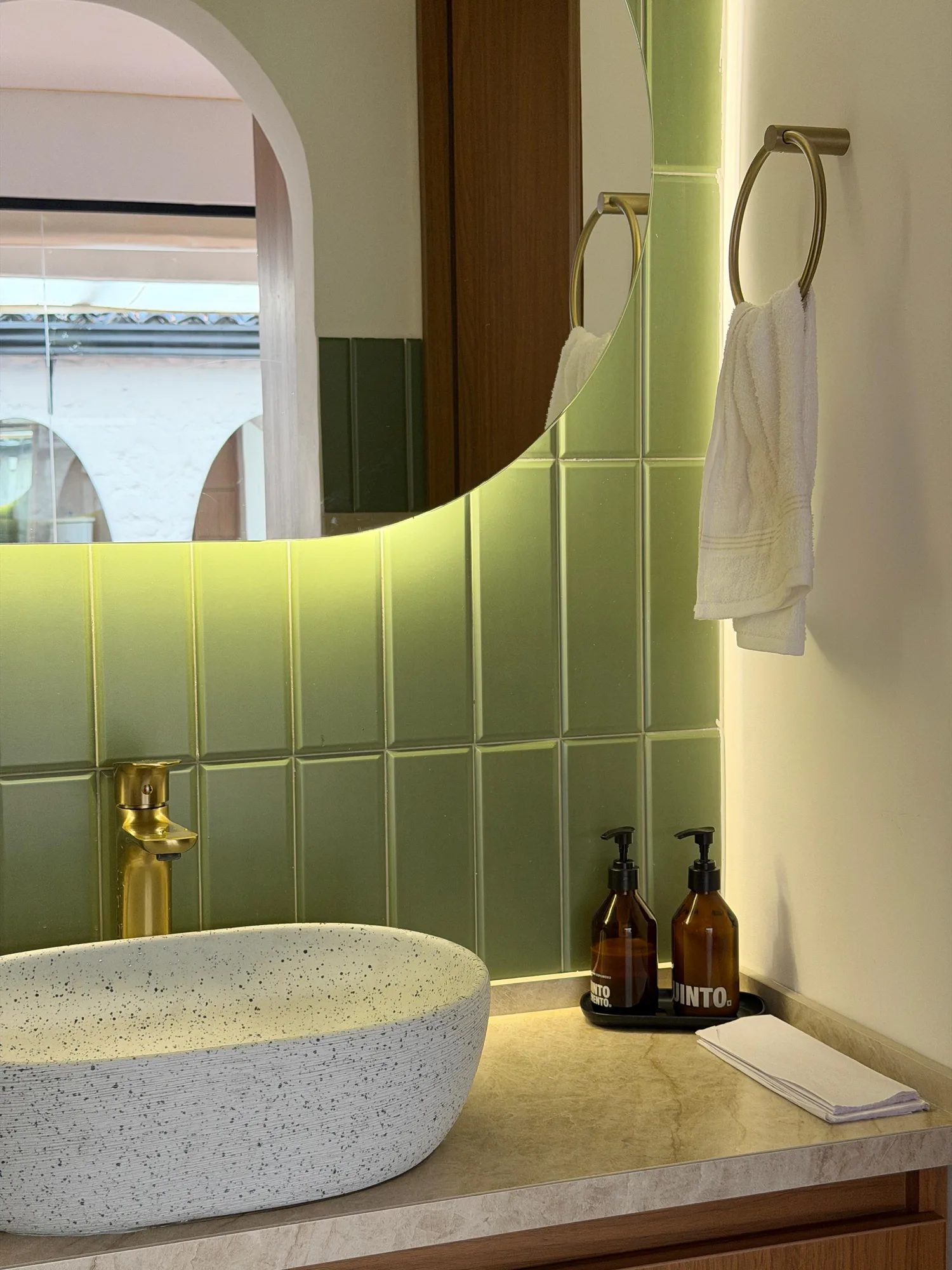 Baño con azulejos verdes, espejo iluminado y lavamanos de piedra