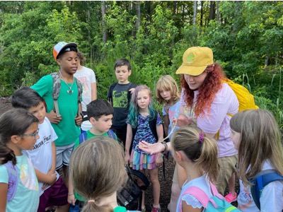 A naturalist counselor showing a group of camper students something in nature, perhaps a snake skin.