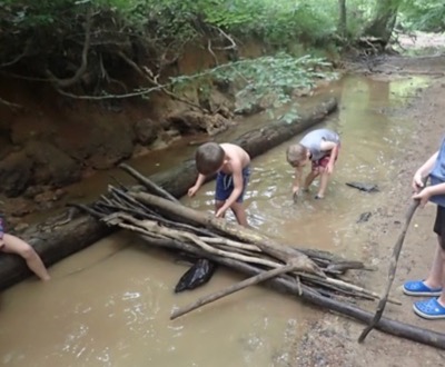Campers building a makeshift dam in a muddy creek using long sticks.