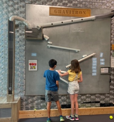 Two campers experimenting with the Gravitron, an interactive display to try balls rolling down inclines in different ways, at Kidzu Children's Museum.