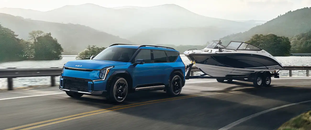 Vue 3/4 avant et latérale du Kia EV9 2025 en puissance sur route tractant un bateau
