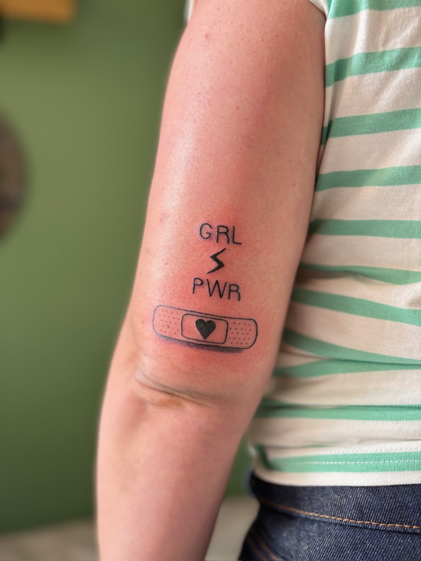 Ce tattoo minimaliste associe le message “GRL PWR”, symbole de force et d’affirmation, à un éclair représentant l’énergi