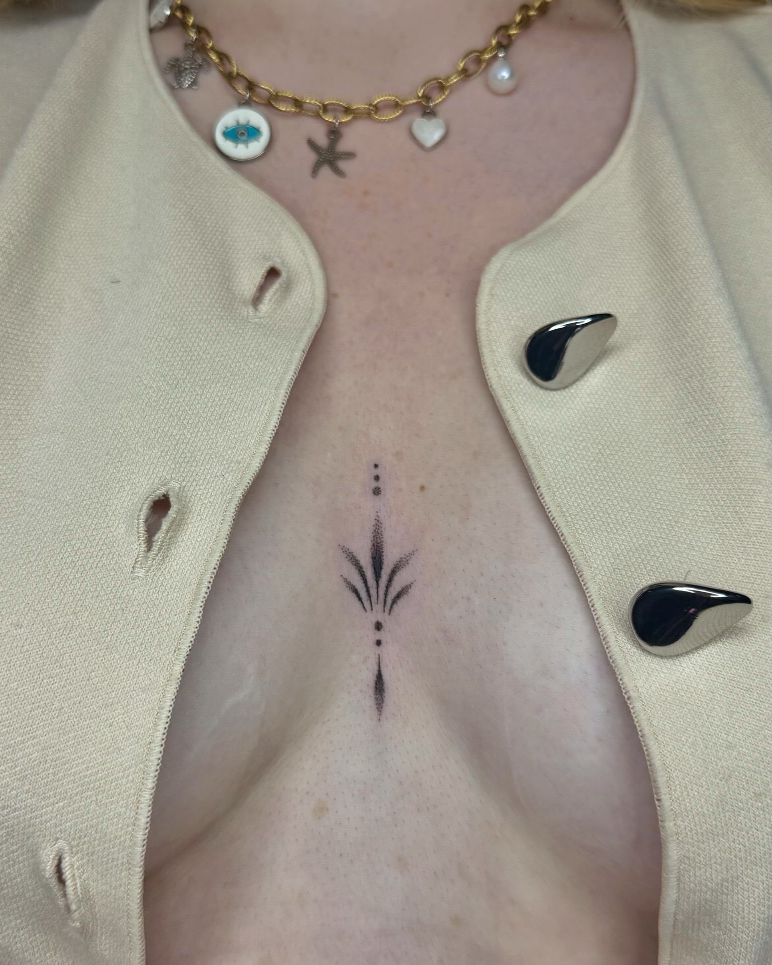 Tatouage minimaliste et élégant entre les seins, réalisé dans un style dotwork.