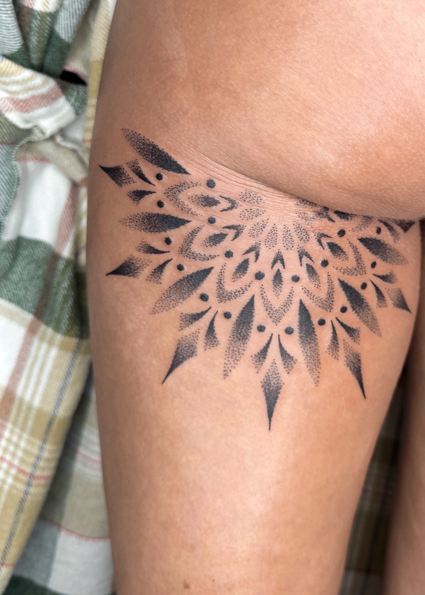 Un tatouage en forme de mandala, situé sous la fesse, réalisé dans un style ornemental raffiné.